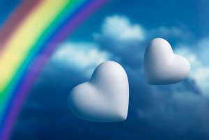 Two hearts and rainbow against a blue sky