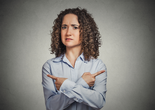 Indecision confusion. Portrait confused young woman pointing in two different directions not sure which way to go isolated grey background. Negative emotion facial expression feeling body language